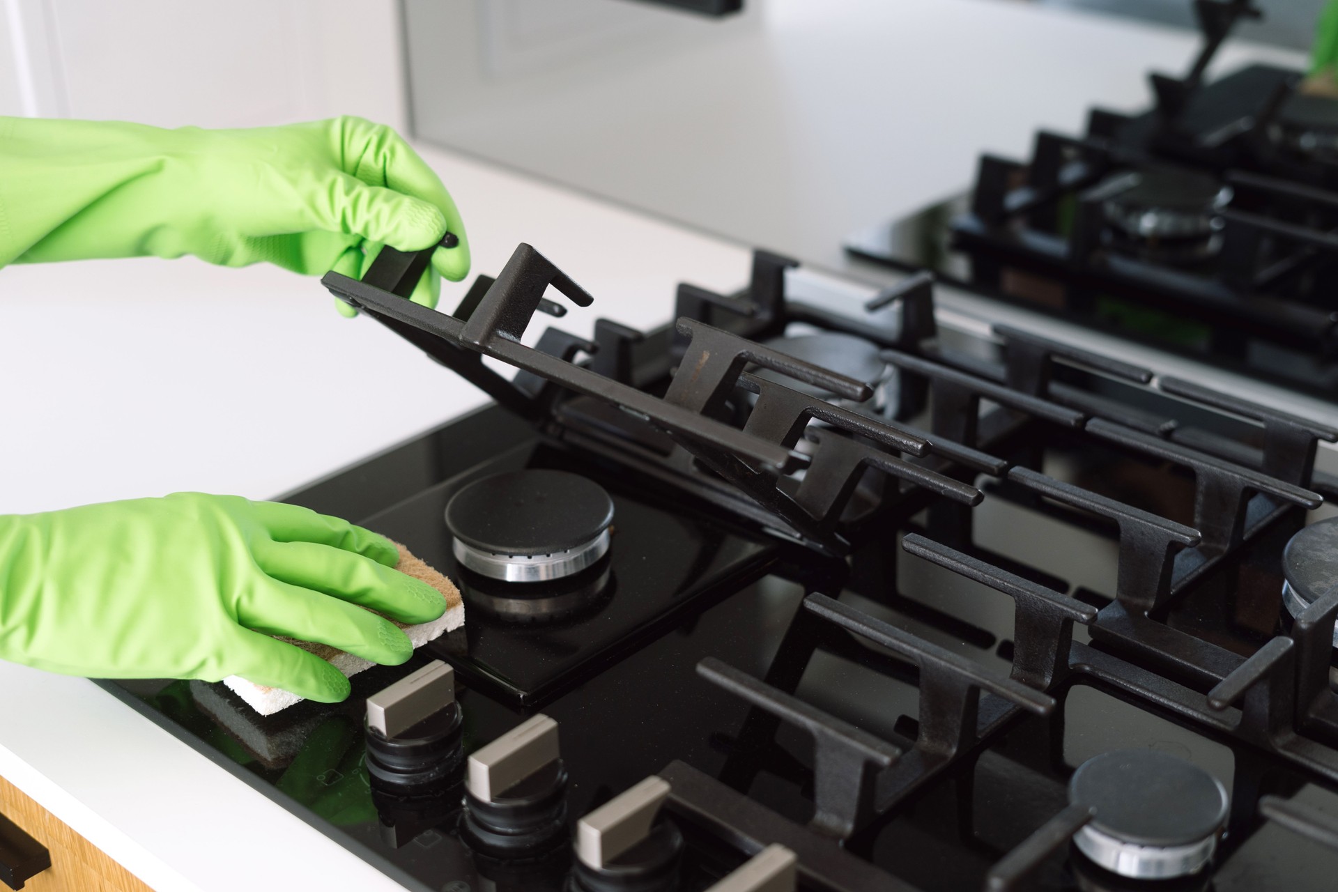 A person in green gloves cleaning a modern gas stove on kitchen