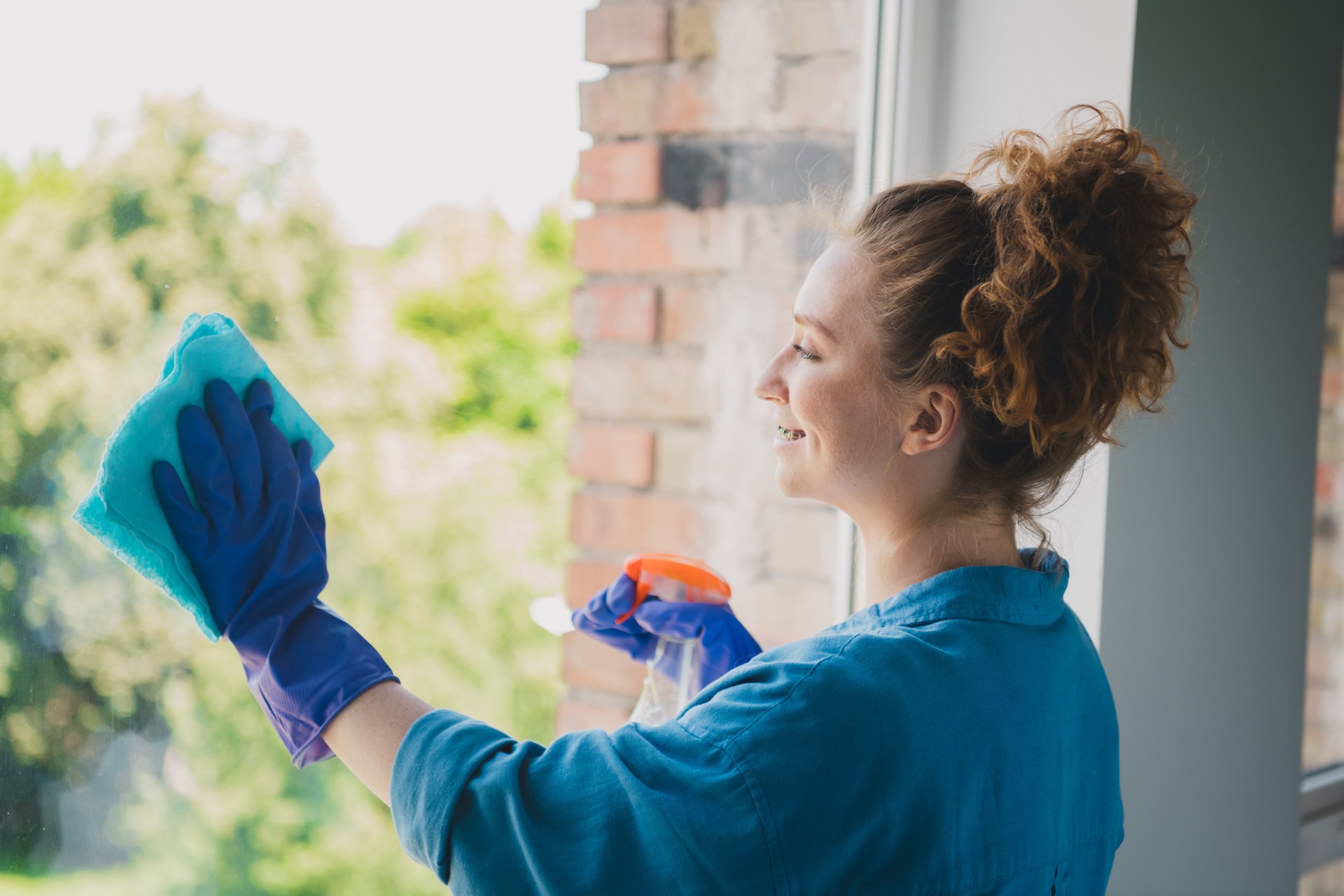 Photo of lovely young ginger girl wipe clean window dressed blue garment spacious house indoors room